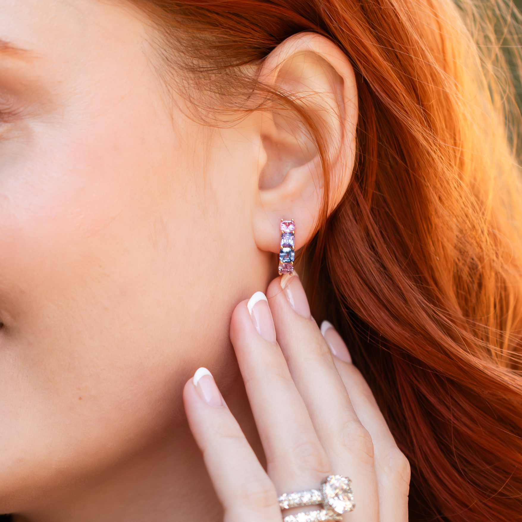 womans hand with diamond ring and band and multi-colored stone huggie earring