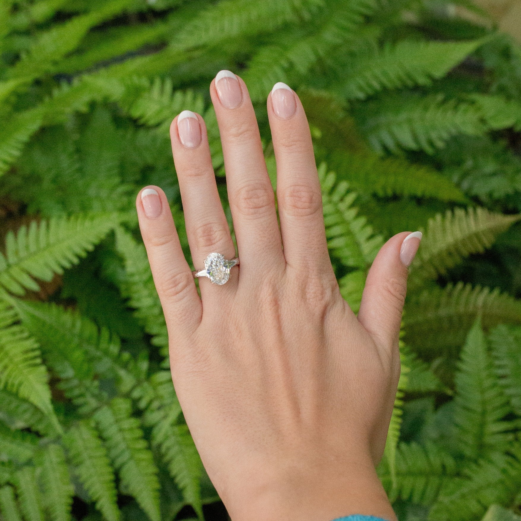 A woman's left hand with a diamond ring on it and trees in the background